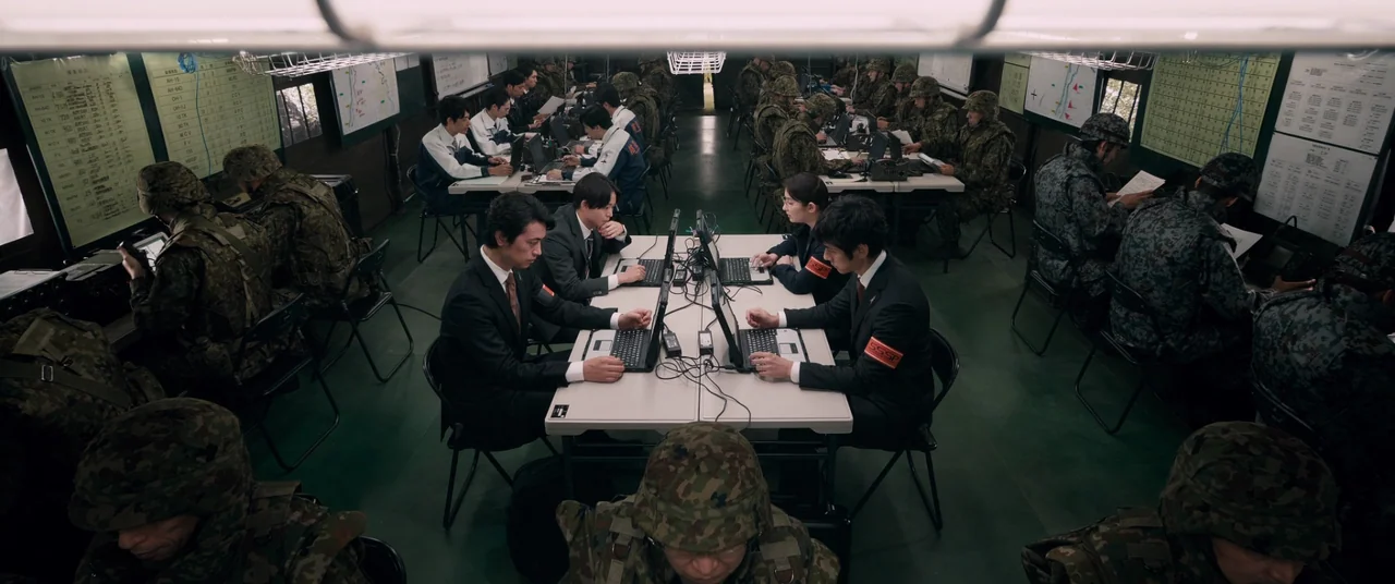 Shin Ultraman (2022) movie still: wide — An interior military command post features multiple rows of tables with personnel using laptops. Military…