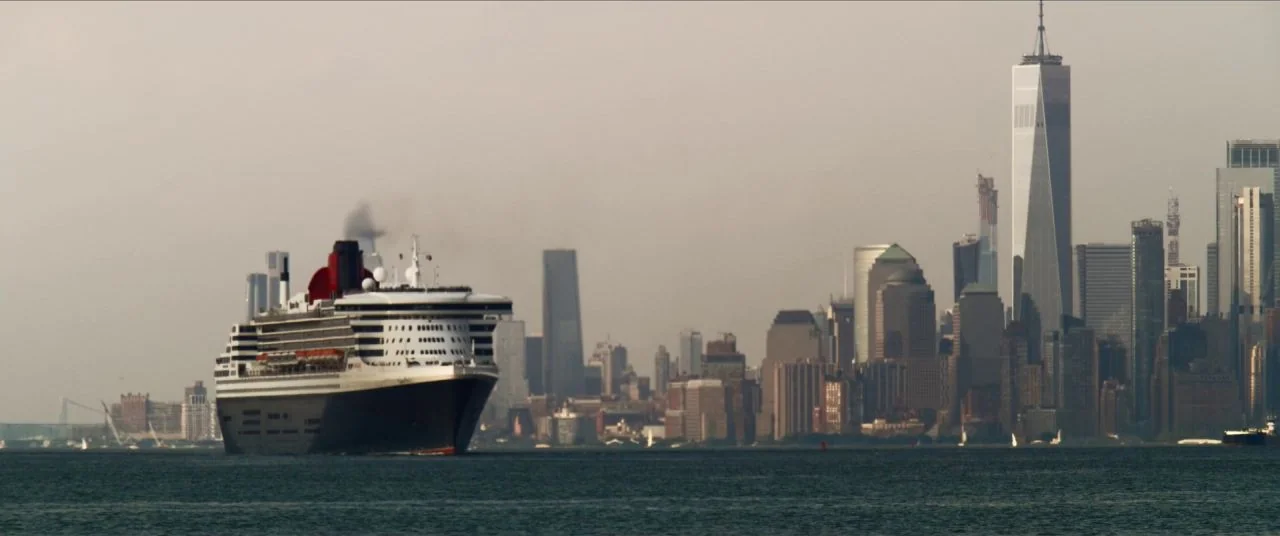 Let Them All Talk movie still: wide — A massive ocean liner glides through a harbor in front of a dense metropolis. The New York City skyline is…