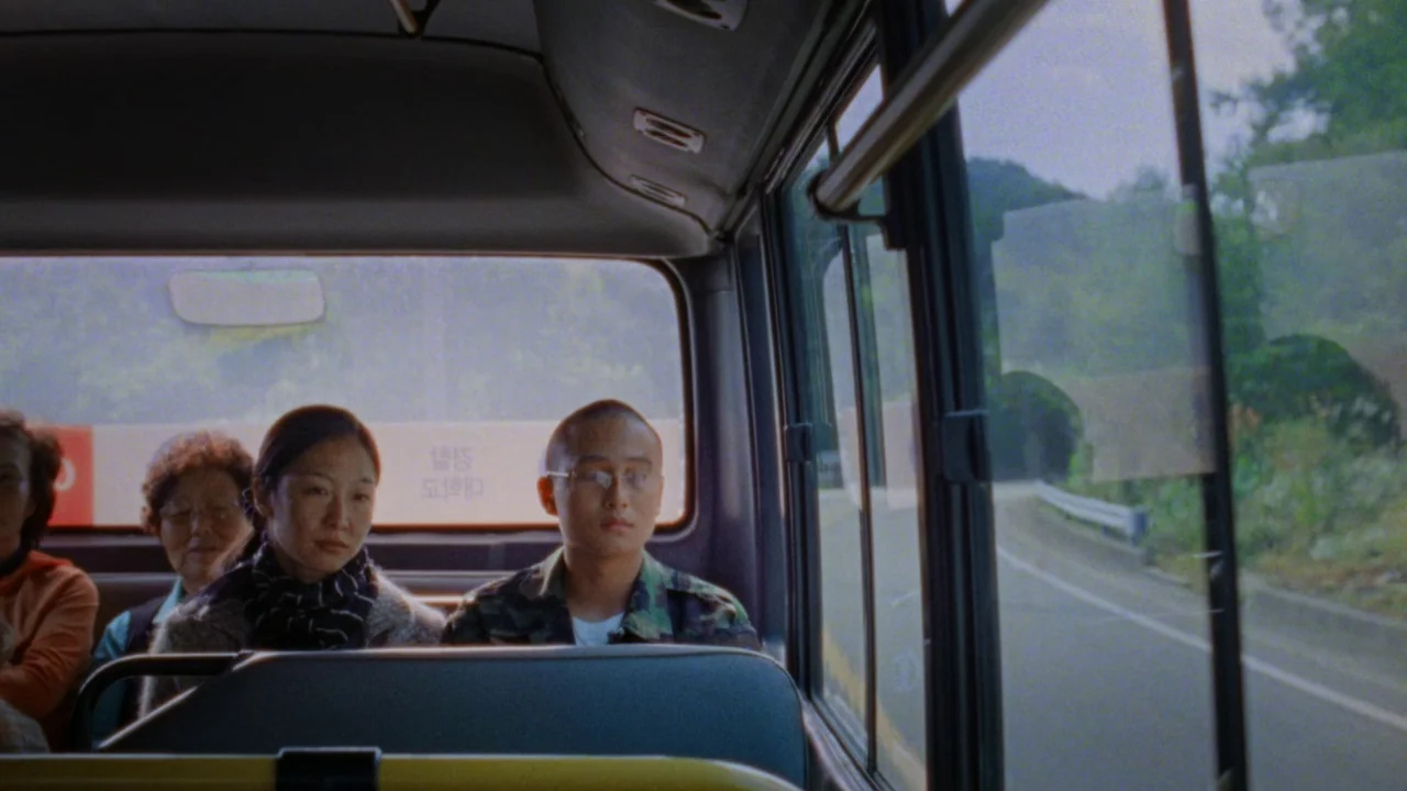 Riceboy Sleeps (2022) movie still: medium — The interior of a bus showing passengers seated against the rear window. A man in military camouflage…