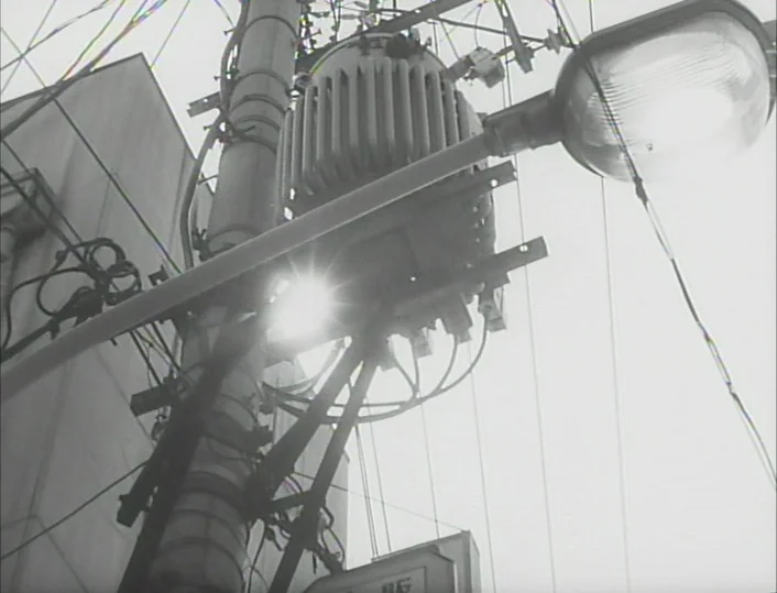Funeral Parade of Roses (1969) movie still: wide — An urban utility pole holds a power transformer and streetlamp against a bright sky. Numerous…