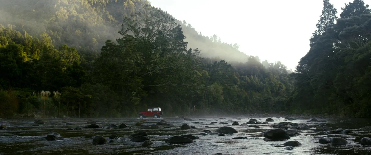 Evil Dead (2013) movie still: wide — A wide, shallow river flows through a dense, mist-filled valley surrounded by evergreen forest. A single small…