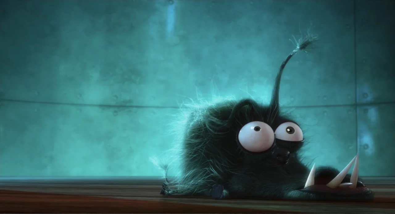Despicable Me (2010) movie still: medium — A small fuzzy creature with large eyes rests on a dark wooden floor against teal metal walls. The…