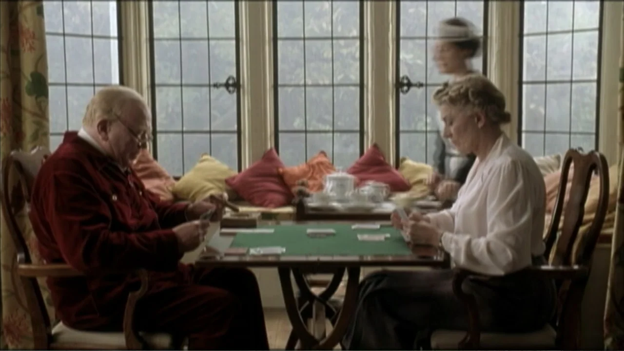 The Gathering Storm (2002) movie still: medium — A 1940s sunroom features large mullioned windows with colorful pillows on a built-in bench. A man…