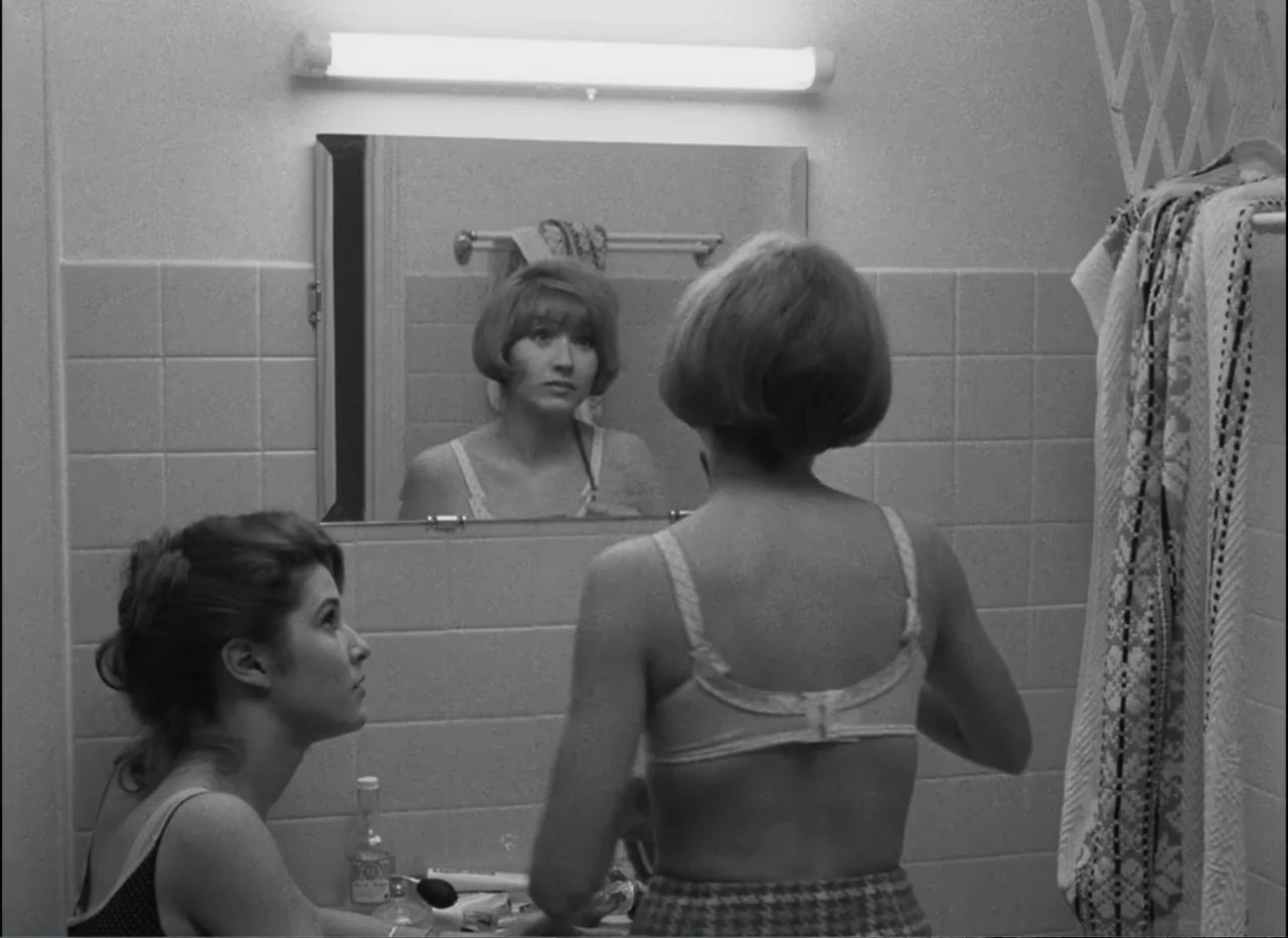 Masculin Féminin (1966) movie still: medium — A tiled bathroom features a large wall mirror above a sink vanity. Two women stand together while one…