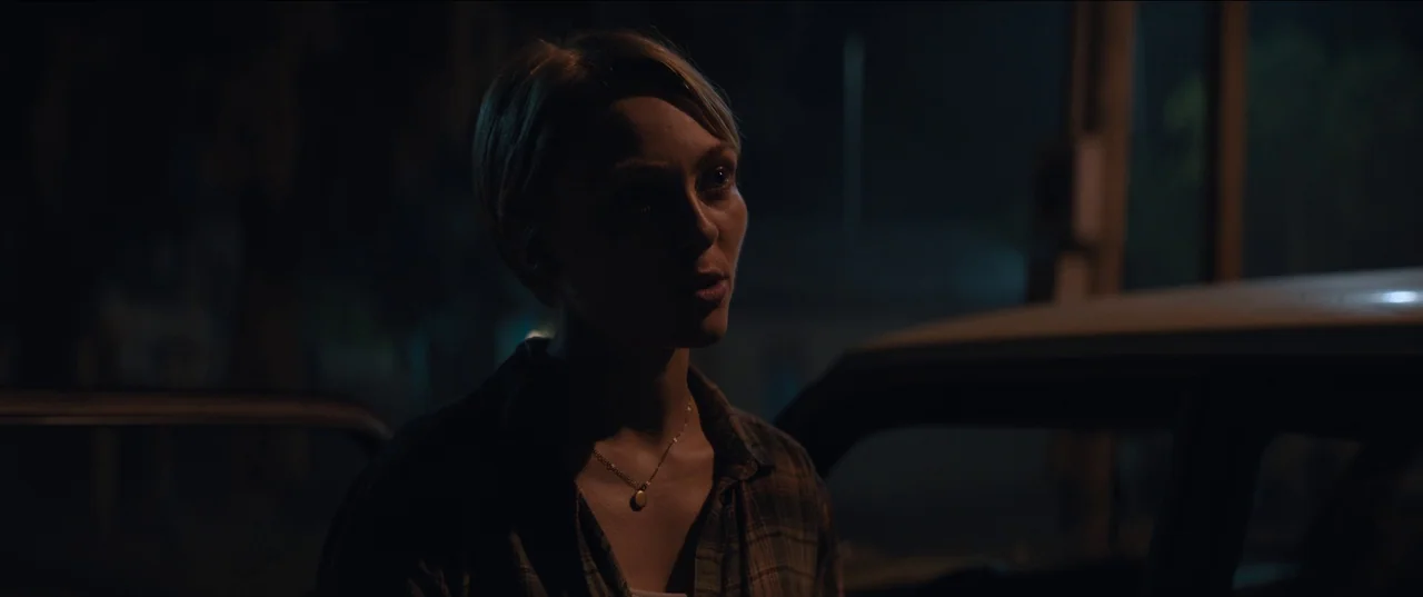 Rebel Ridge (2024) movie still: medium — A dark night setting outdoors with a vehicle partially visible in the frame. A woman stands in the shadows…