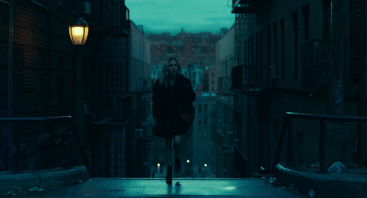 Joker: Folie à Deux (2024) movie still: fullbody — A woman walks up a dark set of concrete stairs between two narrow brick buildings. The background…