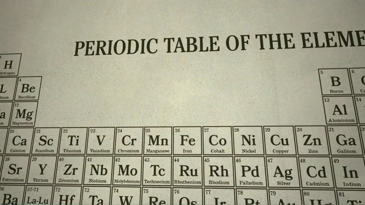 Common Ground (2000) movie still: closeup — A close-up view of a printed periodic table of the elements on parchment paper. The text is sharp and…
