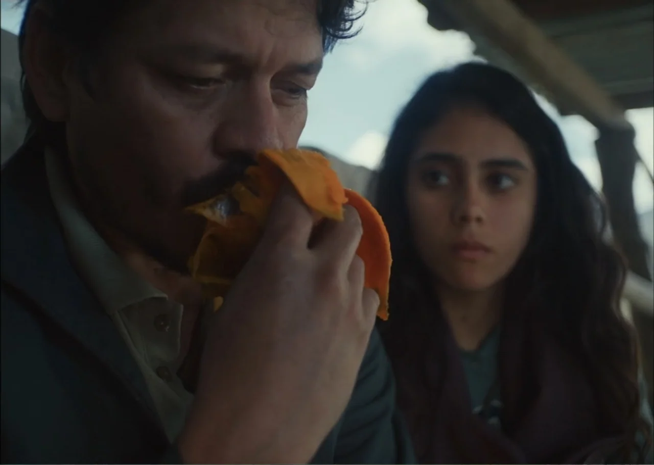 A Fisherman's Tale (1976) movie still: medium — A man and a girl sit on a covered porch in natural daylight. The man holds an orange fruit to his…