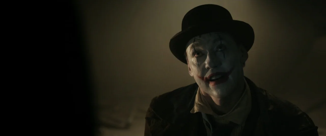 Clown in a Cornfield (2025) movie still: closeup — A dark, dimly lit interior room serves as the setting for the subject. A man wearing clown makeup…