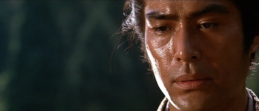 Lone Wolf and Cub: Baby Cart to Hades (1972) movie still: closeup — An outdoor area with dark foliage visible in the out-of-focus background. A man…