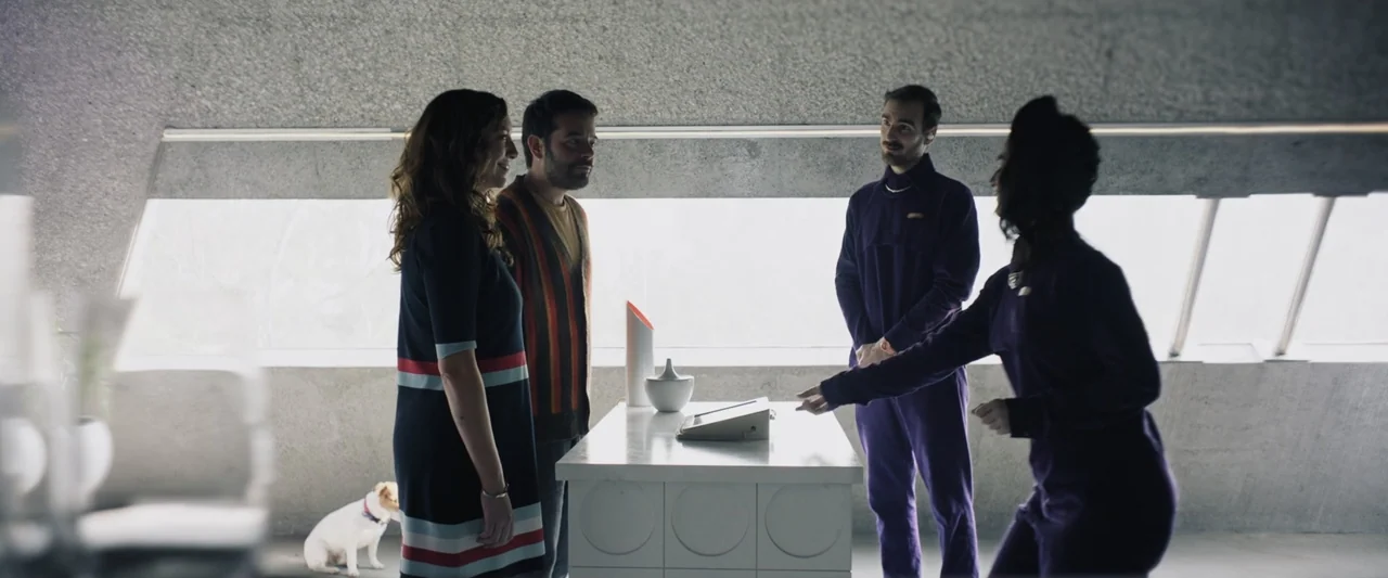 Sign Here (2017) movie still: fullbody — A minimalist room features unfinished concrete walls and a long horizontal window. Four people stand around…