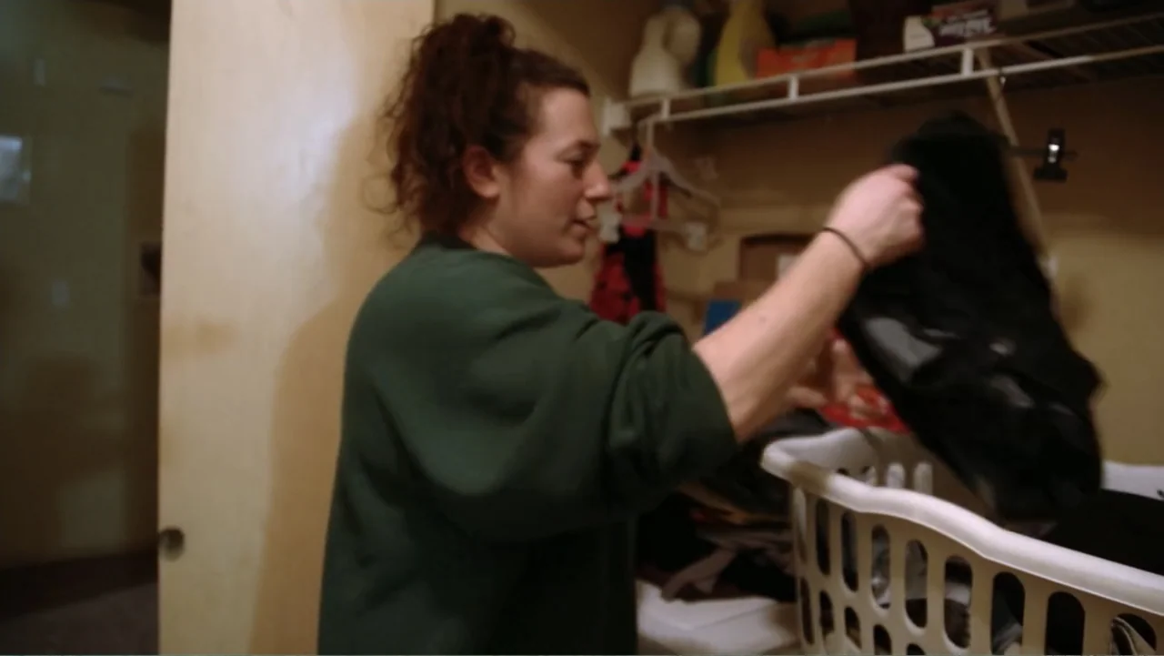 A Dangerous Son (2018) movie still: medium — A small closet with shelves and hanging racks contains miscellaneous clothing and plastic containers. A…