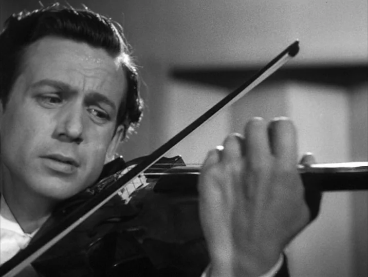 To Joy (1950) movie still: closeup — A dimly lit interior space serves as the backdrop for a formal musical performance. A man plays the violin with…