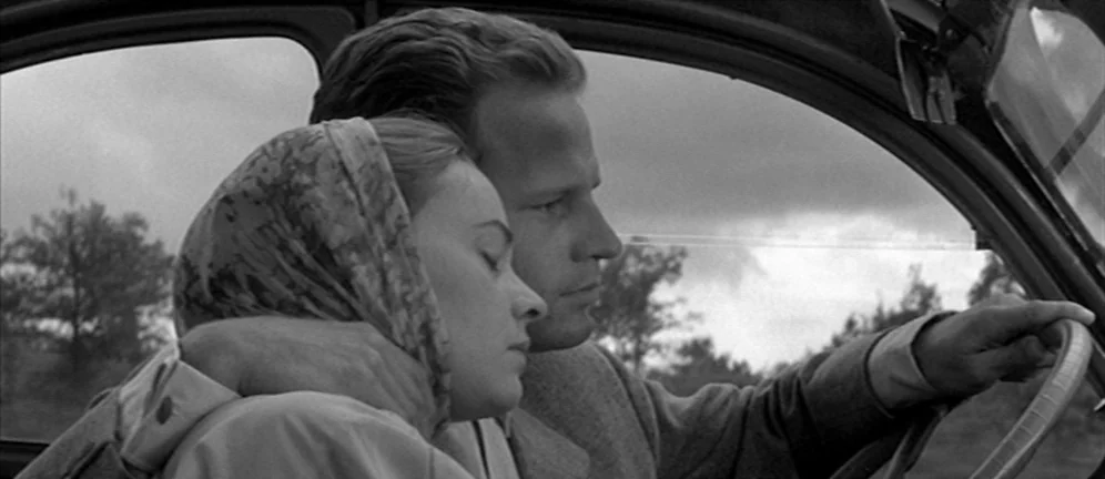 Les Amants (1958) movie still: medium — The interior of a moving 1950s car shows the driver and a passenger. A man steers the vehicle while a woman…
