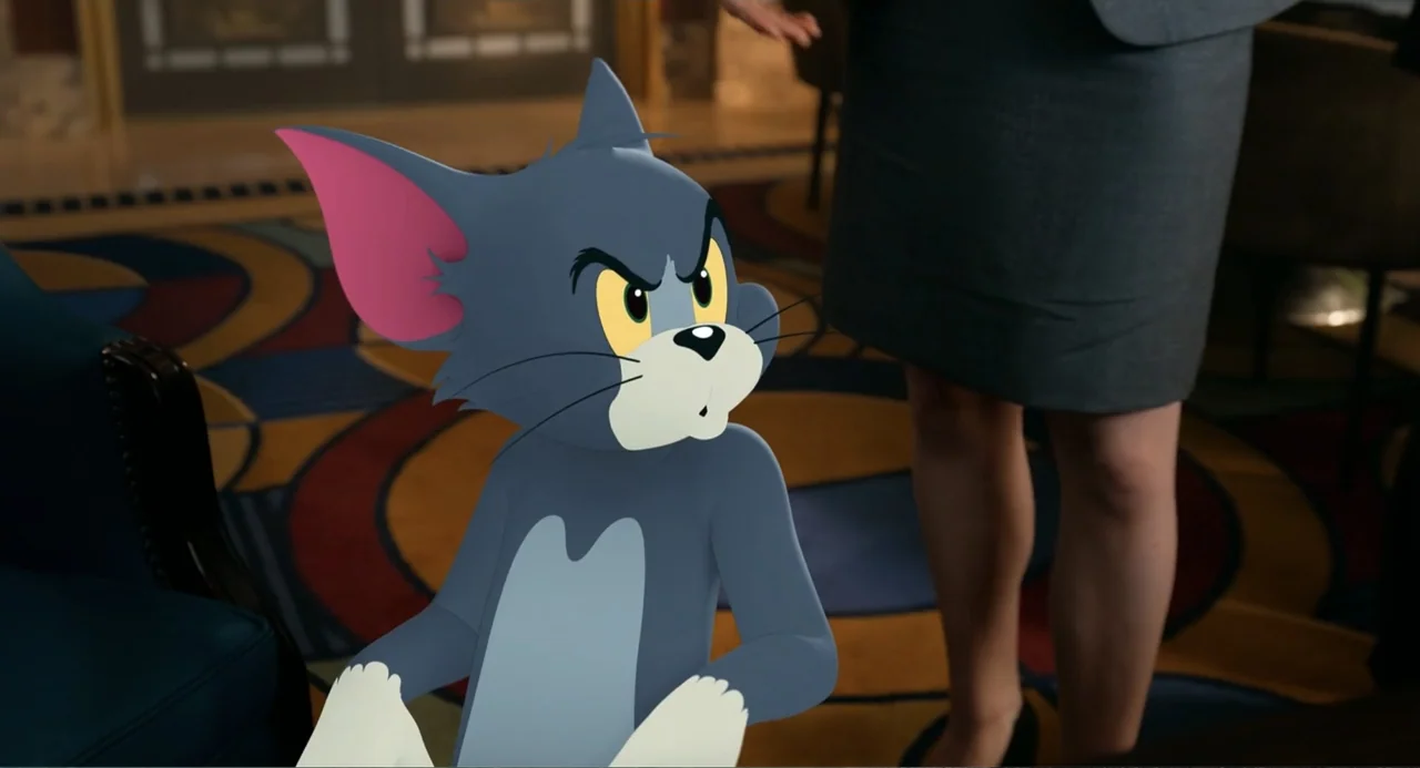 Tom & Jerry (2021) movie still: medium — An indoor hotel lobby with patterned carpeting and a person standing in the background. A cartoon cat…