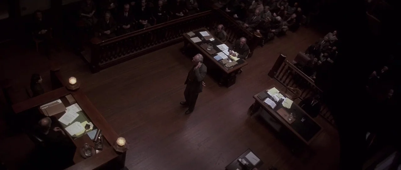 Snow Falling on Cedars (1999) movie still: wide — A dark wooden courtroom features rows of spectators and multiple tables for legal counsel. A lone…