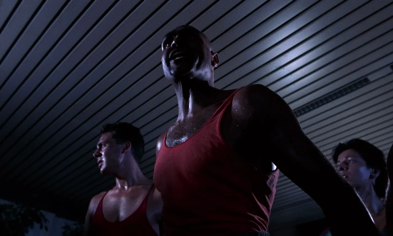 Demons 2 (1986) movie still: medium — An indoor swimming pool area features ribbed white ceiling panels above the athletes. Three sweaty people in…