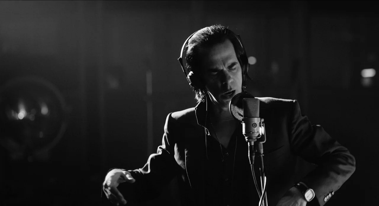One More Time With Feeling movie still: medium — A dark recording booth is filled with shadows and minimal equipment. A man wearing headphones…
