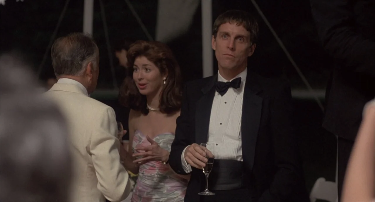 Masquerade (2023) movie still: medium — A group of people in formal attire stand together at an outdoor evening gathering. A man in a tuxedo holds a…