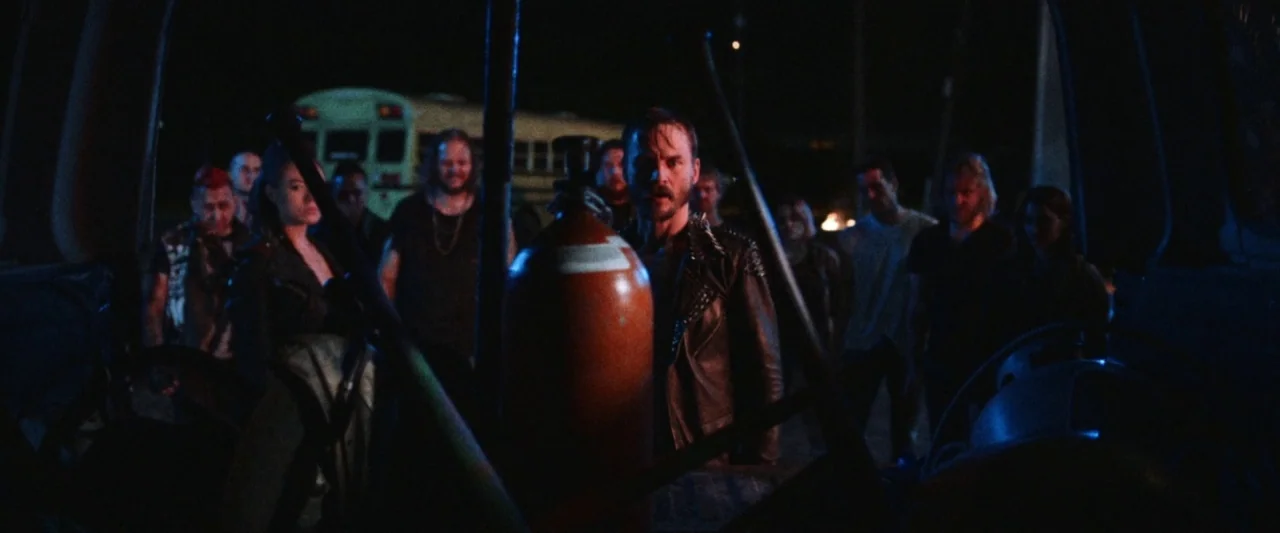 VFW movie still: medium — A group of people stands in a dark parking lot near an industrial vehicle. A large red pressurized gas tank sits in the…