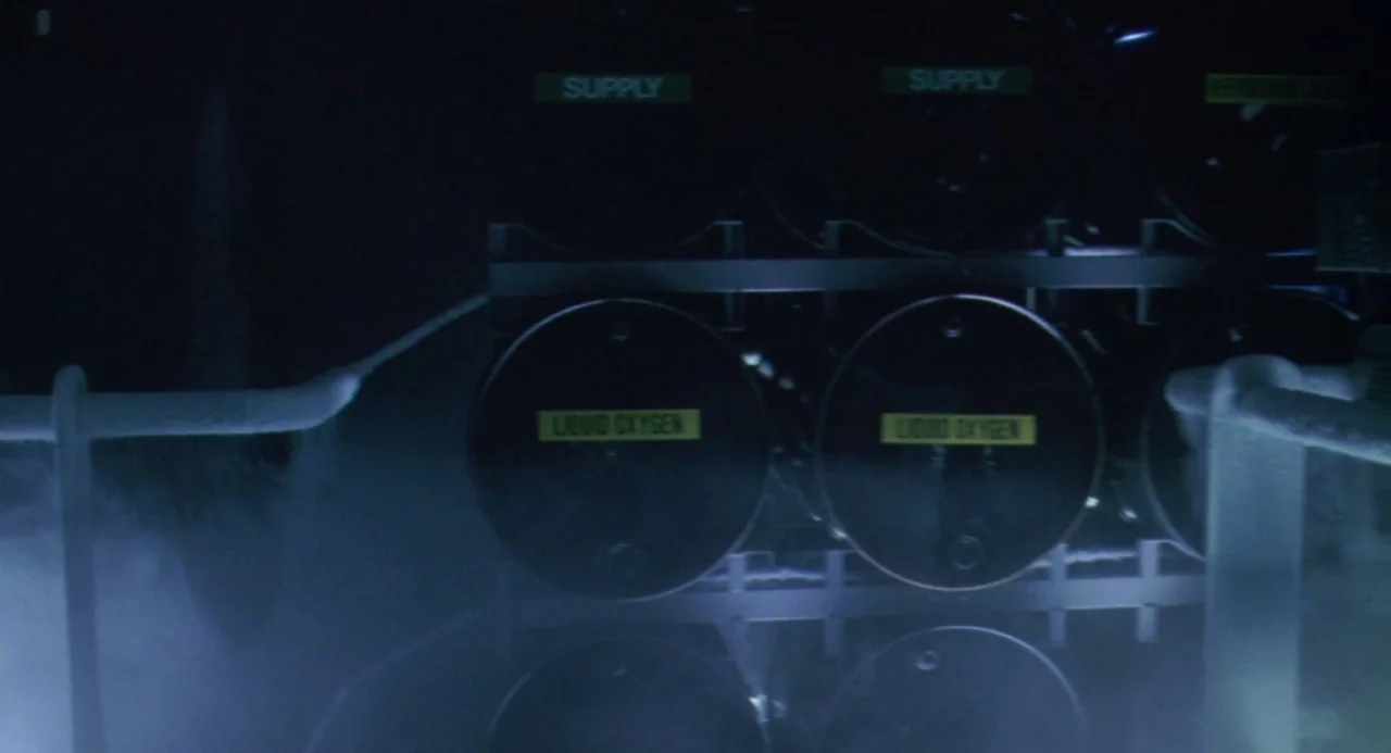 Universal Soldier: The Return (1999) movie still: medium — A dark industrial space contains several large black tanks labeled liquid oxygen. Dense…