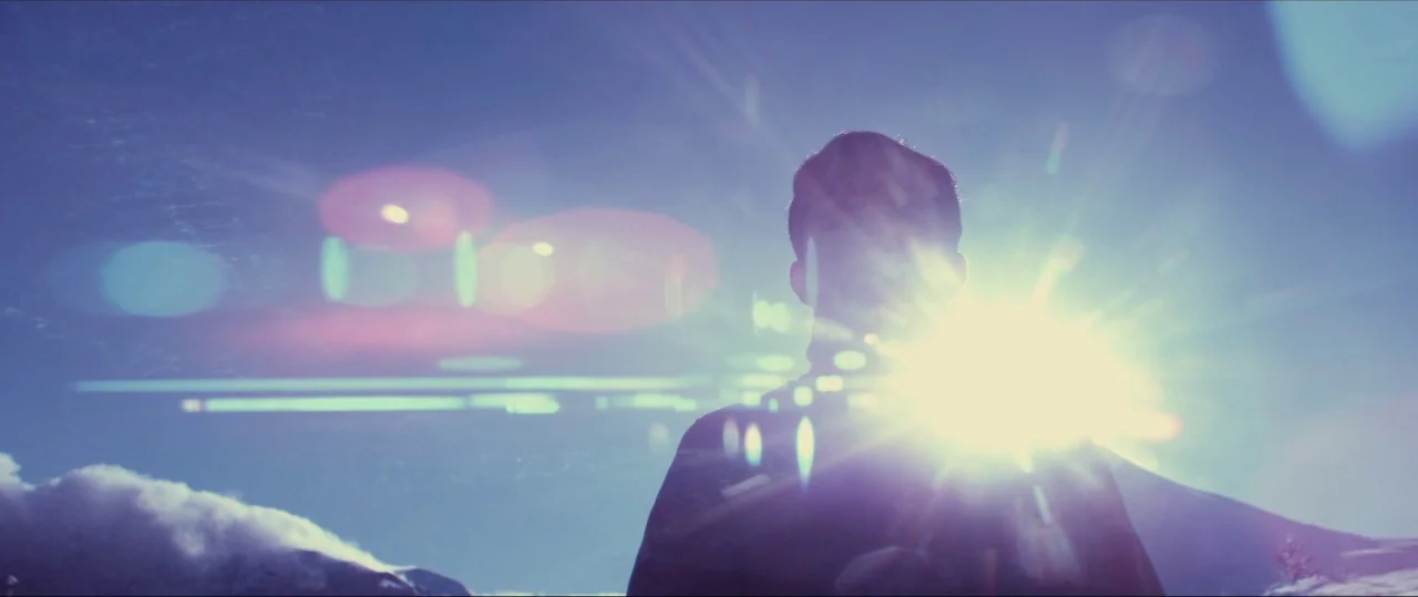 Neruda (2016) movie still: medium — A figure stands on a snowy or clouded mountain slope against a bright sky. The sun is positioned directly behind…