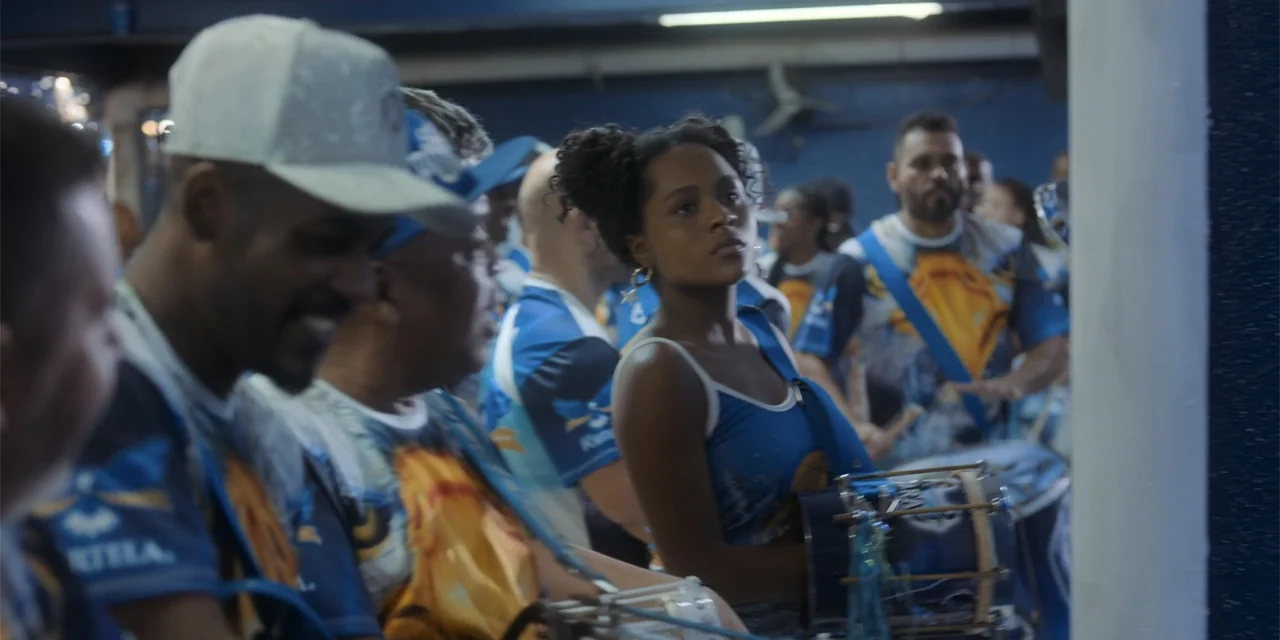 An Unforgettable Year - Summer (2023) movie still: medium — A crowded indoor space features a group of musicians dressed in matching blue outfits. A…