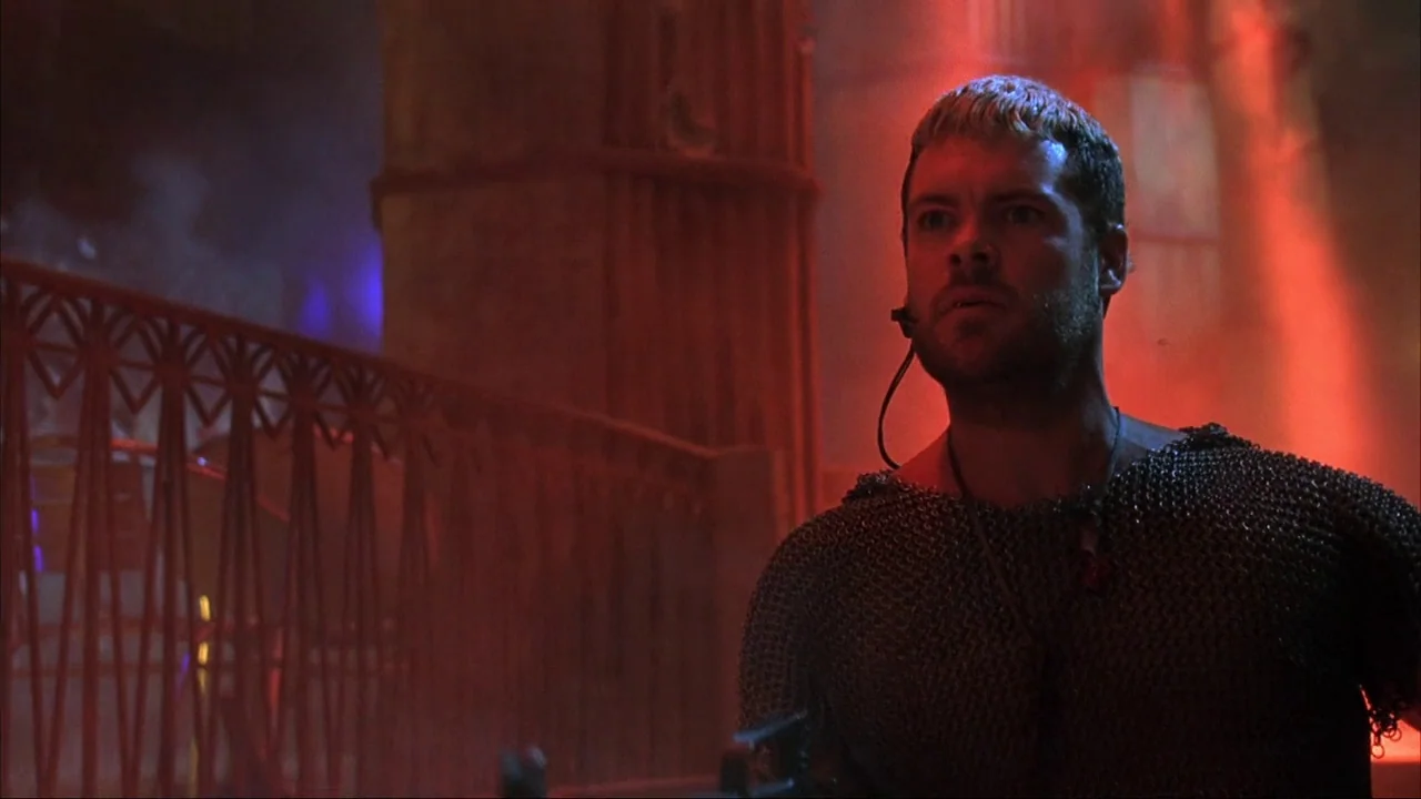 Blade II (2002) movie still: medium — A dimly lit club interior featuring red ambient lighting and decorative metal railing structures. A man…