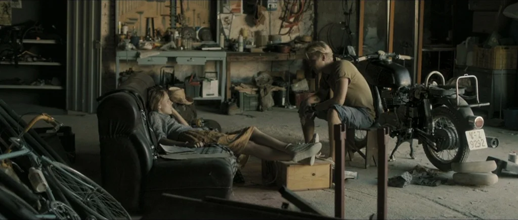 Lasting (Nieulotne) (2013) movie still: wide — A cluttered garage workspace is filled with miscellaneous tools, bicycles, and storage crates. A…