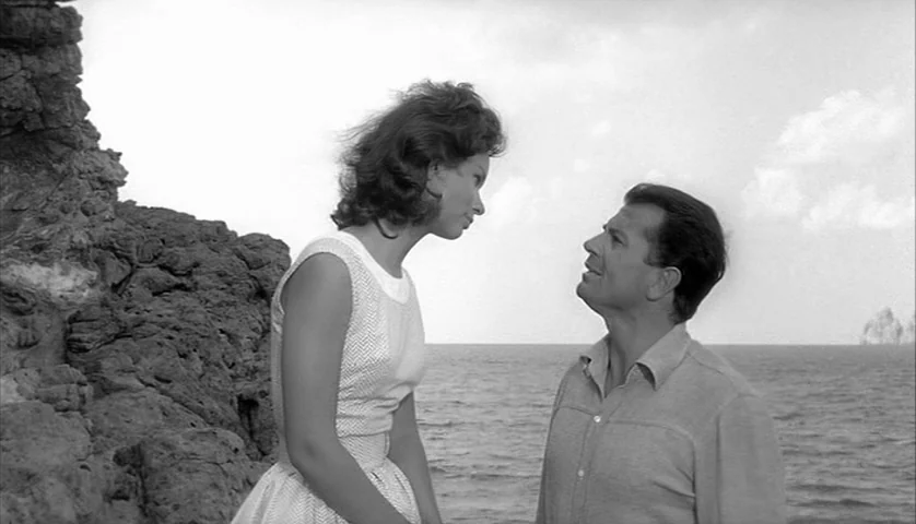 L’Avventura (1960) movie still: medium — A rocky coastal cliff overlooks the open sea under a bright, overcast sky. A woman stands in profile while…