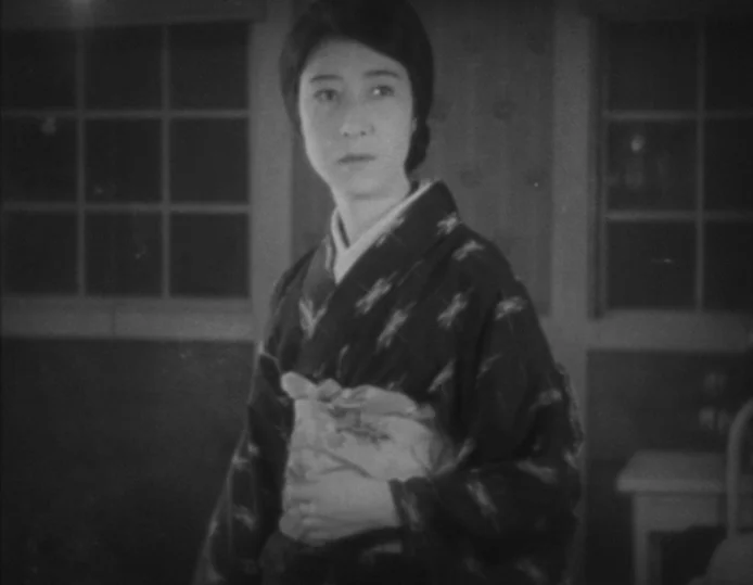 Tokyo Chorus (1931) movie still: medium — The interior of a traditional Japanese home features paper sliding doors in the background. A woman in a…