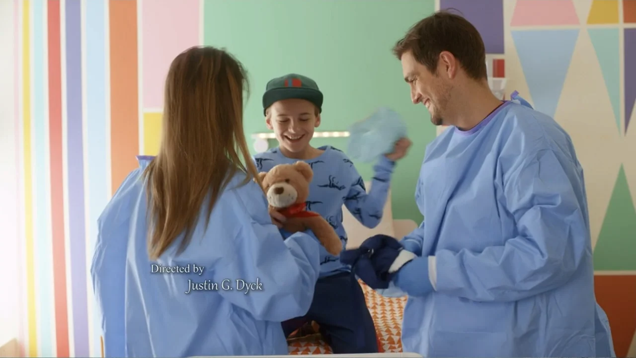 Christmas with a Prince (2018) movie still: medium — A colorful hospital room features pastel-striped walls and a patterned bedspread. A child plays…