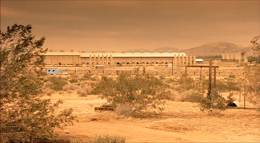 Erin Brockovich (2000) movie still: establishing — An industrial facility with multiple silos sits across a dry, sparse desert scrub plain. A small…