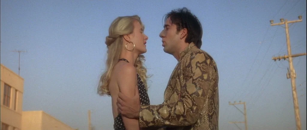 Wild At Heart (1990) movie still: medium — A flat desert landscape features a wooden power line pole in the background. A woman in a polka dot top…