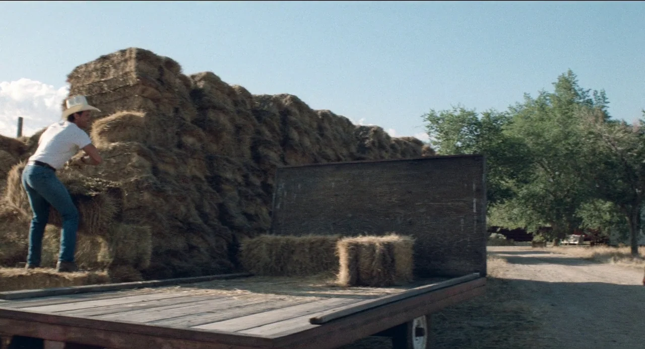 Desert Hearts (1985) movie still: medium — A rural setting features a wooden flatbed trailer loaded with square hay bales. A man in a cowboy hat…