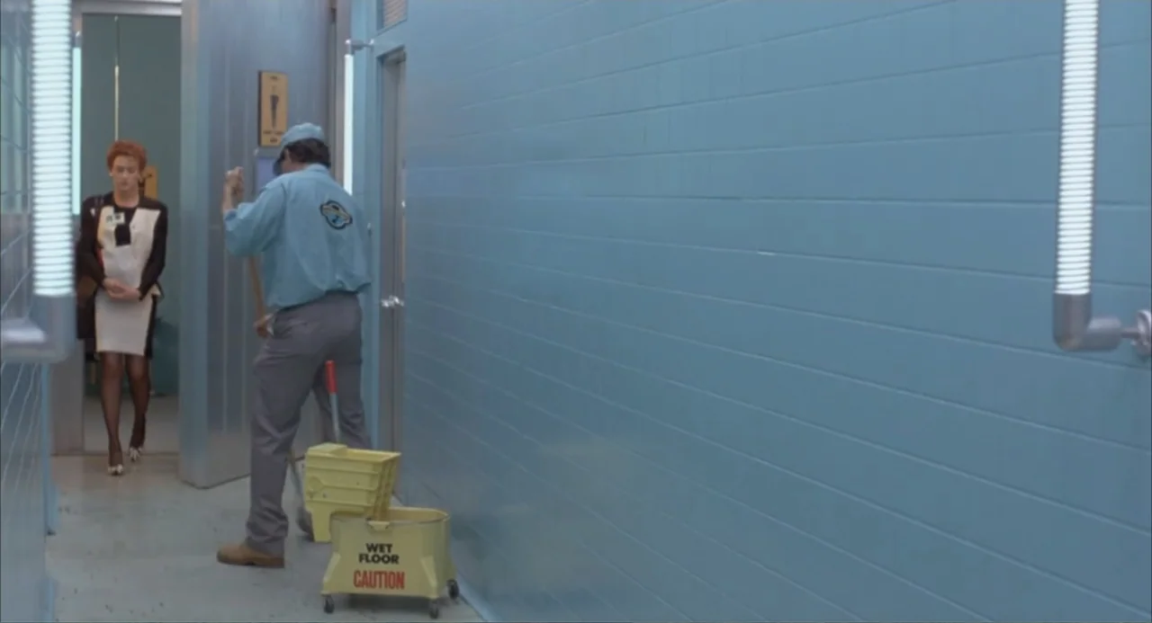 Making Mr. Right (1987) movie still: fullbody — A hospital or office corridor with light blue tile walls and industrial flooring. A janitor in a…