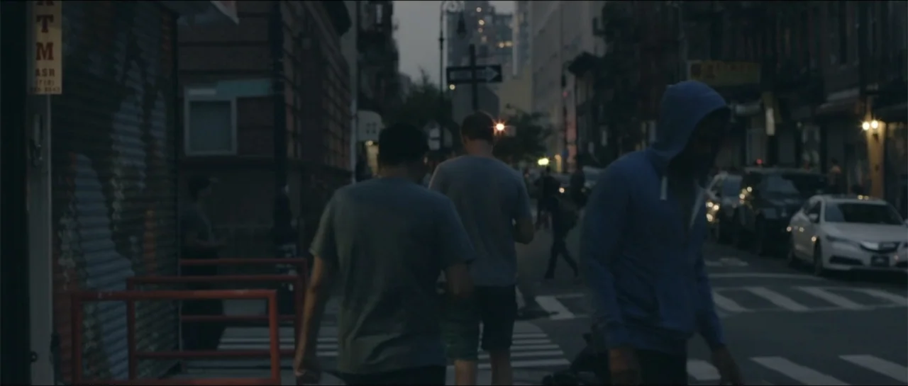 All She Wrote (2018) movie still: medium — An urban intersection at dusk features three men walking away from the camera. Low light conditions show…