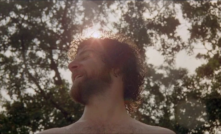 Yentl (1983) movie still: closeup — A man stands outdoors under a canopy of dense, blurred green tree leaves. The sun shines directly from behind…