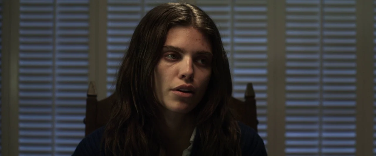 Excision (2012) movie still: closeup — A dark, interior room features closed window shutters in the blurred background. A young woman with long…