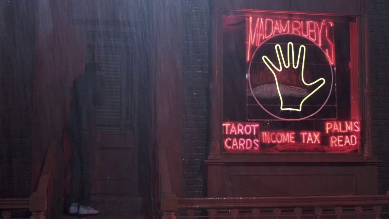 Pee-Wee’s Big Adventure (1985) movie still: fullbody — A brick storefront displays a neon sign advertising tarot cards and palms being read. A man…
