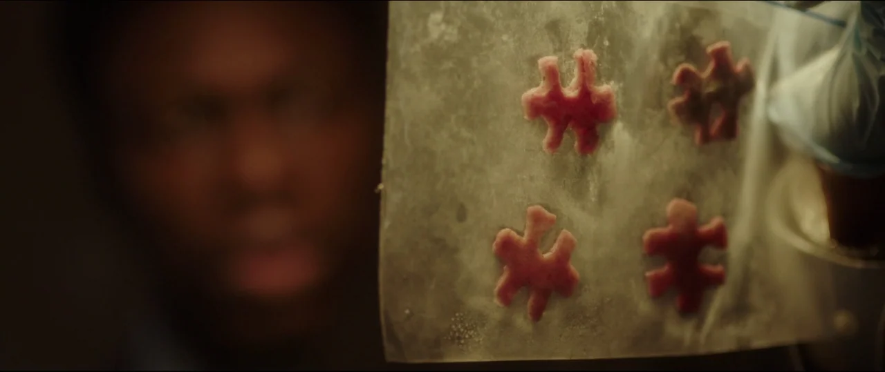 Jigsaw (2017) movie still: closeup — A dimly lit interior space with a person in the background out of focus. A hand wearing a blue medical glove…