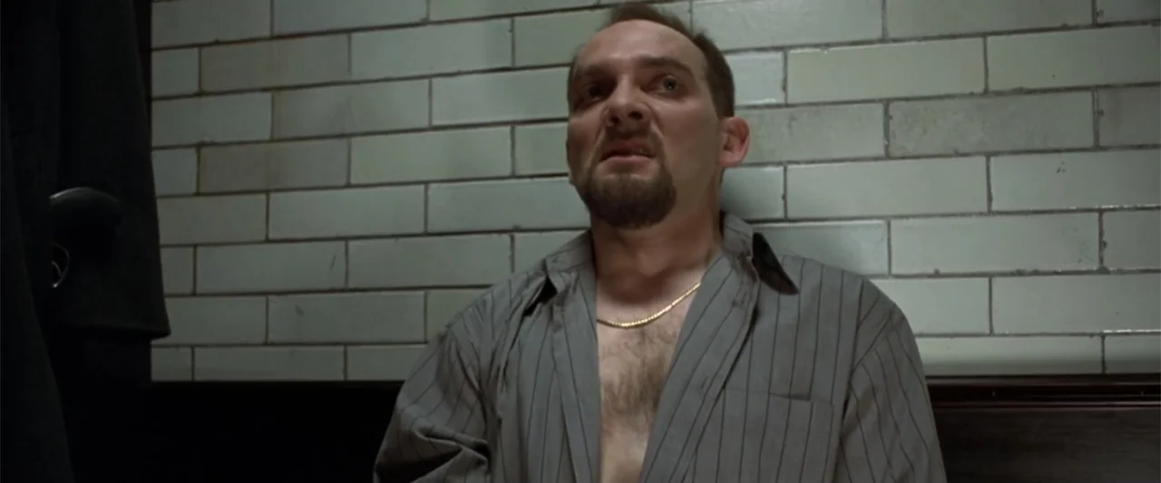 Maximum Risk (1996) movie still: medium — An interior space features white tiled walls and dark trim. A man in an open pinstriped shirt stands…