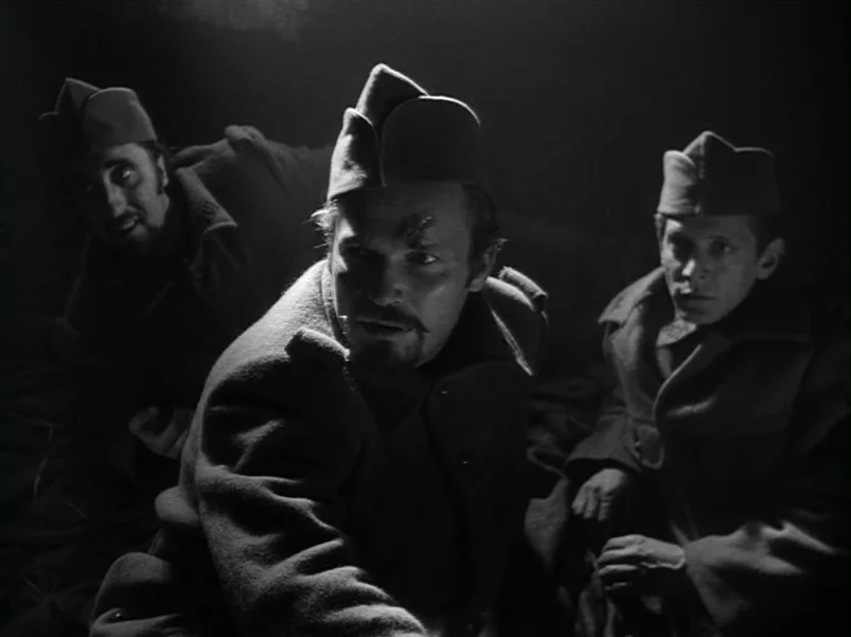 Paths of Glory (1957) movie still: medium — A dark, cramped dugout provides shelter for three soldiers during the night. The men huddle together in…