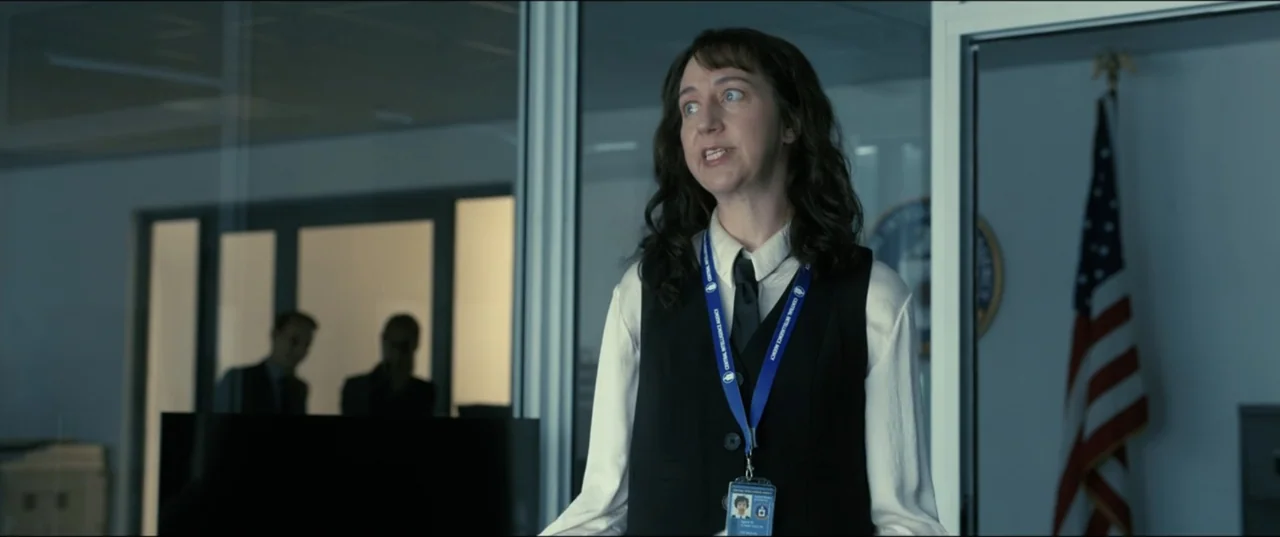 My Spy The Eternal City (2024) movie still: medium — A modern government office featuring glass partitions and an American flag on the wall. A woman…