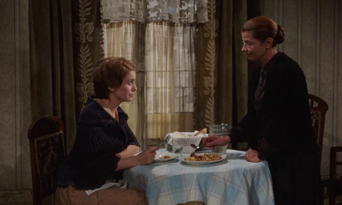 Tristana (1970) movie still: medium — A modest dining area features patterned wallpaper, dark green curtains, and a lace-covered window. An older…