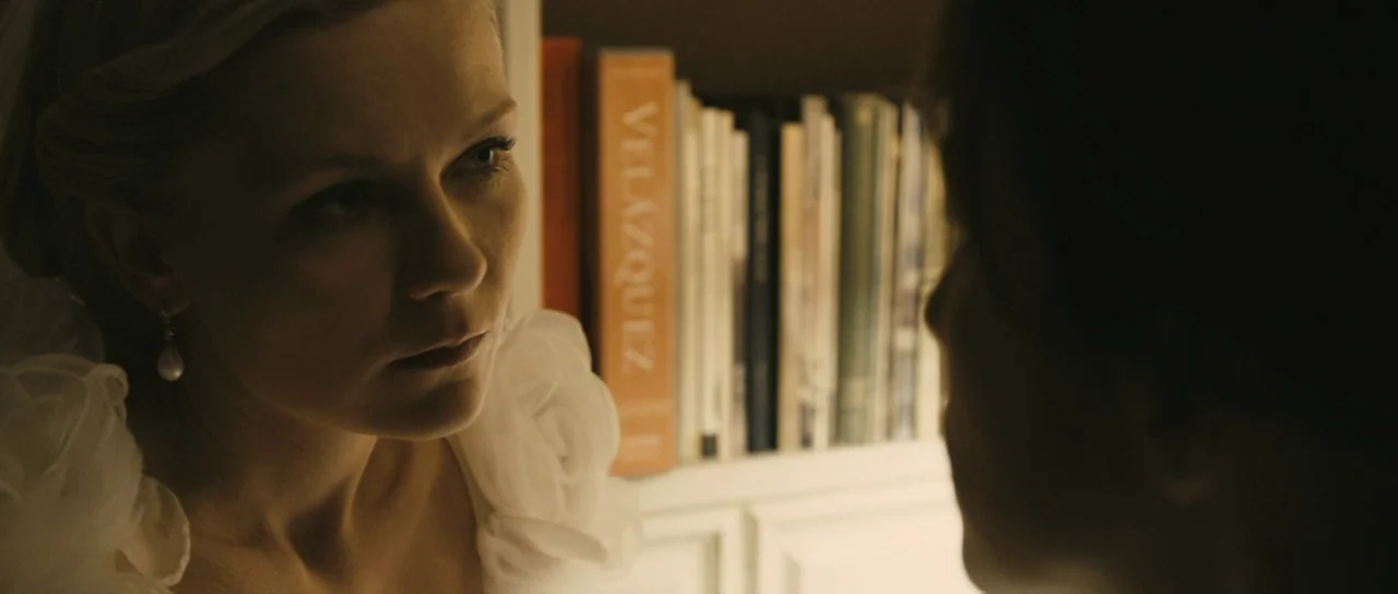 Melancholia (2011) movie still: closeup — A bookshelf filled with books, including one titled Velazquez, sits behind a woman. The woman in the white…