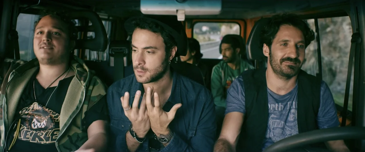 Taranta On the Road (2017) movie still: medium — A group of men travel together inside a vehicle during a daylight commute. The men sit in the front…