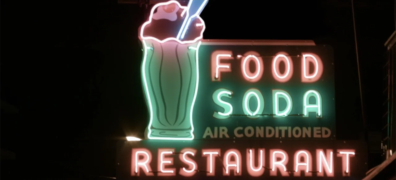 Hellbreeder (2004) movie still: establishing — A vintage exterior neon restaurant sign displays text and a graphic of a milkshake. The sign…