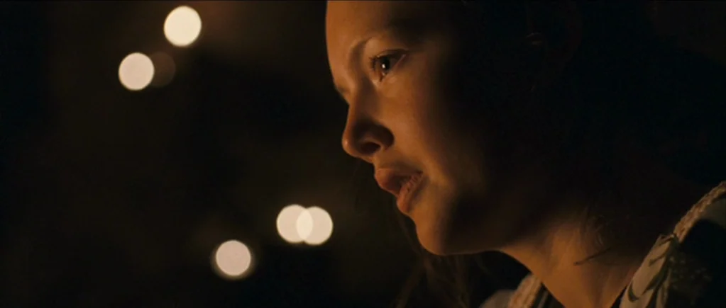 The Scouting Book for Boys (2009) movie still: closeup — A person is lit in a dark room with blurred light bokeh in the background. The subject…