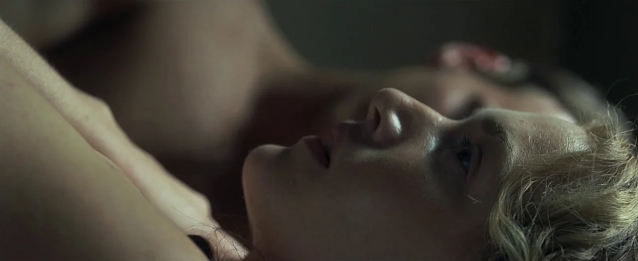 Little Children (2006) movie still: closeup — A close-up view of two people lying together in a dimly lit space. They are positioned face to face…